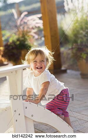 Stock Image - Caucasian baby boy climbing adirondack chair on patio. Fotosearch