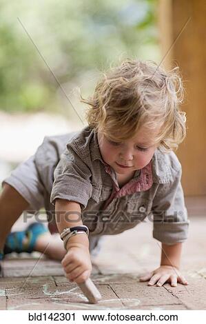 Stock Image - Caucasian baby boy drawing with chalk on brick patio. Fotosearch