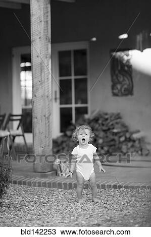 Stock Image - Caucasian baby boy standing on gravel in backyard. Fotosearch