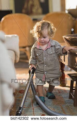 Stock Image - Caucasian baby boy vacuuming living room rug. Fotosearch