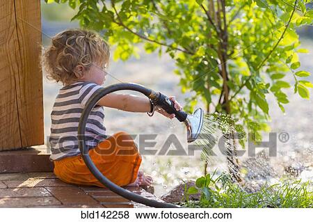 Stock Photo - Caucasian baby boy watering plants from back patio. Fotosearch