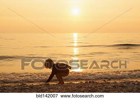 Stock Photo - Caucasian boy playing on rocky beach at sunset. Fotosearch
