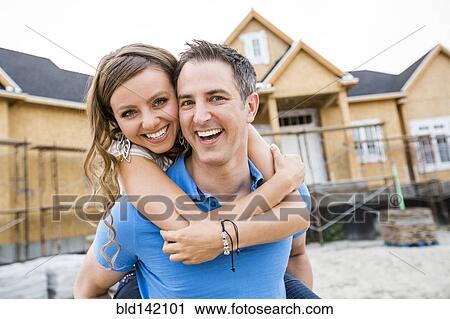 Stock Image - Caucasian couple hugging near house under construction. Fotosearch
