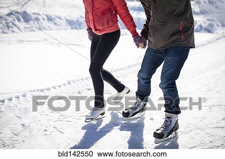 Stock Image - Caucasian couple ice skating on snowy frozen lake. Fotosearch