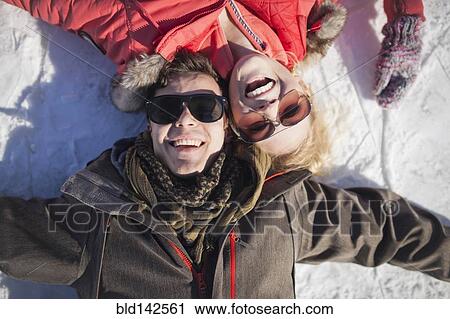 Stock Image - Caucasian couple in sunglasses smiling in snow. Fotosearch