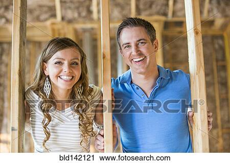 Stock Image - Caucasian couple smiling in house under construction. Fotosearch