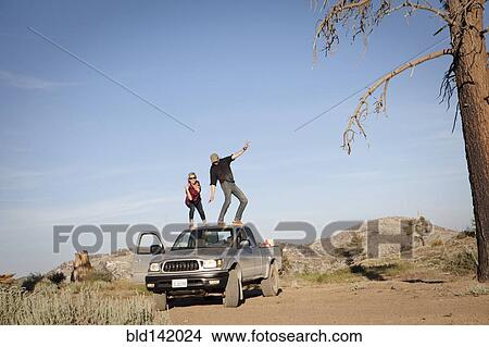 Picture - Caucasian couple standing on roof of pickup truck. Fotosearch