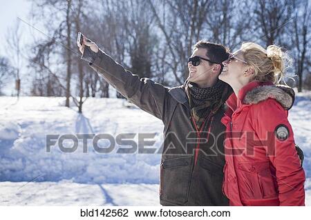 Stock Image - Caucasian couple taking cell phone selfie in winter. Fotosearch