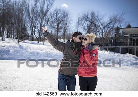 Stock Image - Caucasian couple taking cell phone selfie in winter. Fotosearch