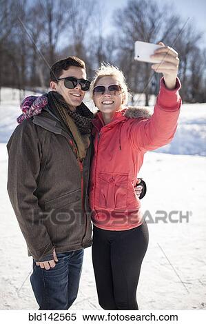Stock Photography - Caucasian couple taking cell phone selfie in winter. Fotosearch