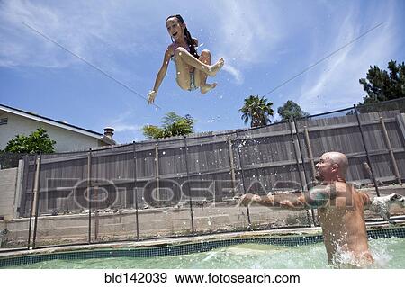 Stock Photo - Caucasian father throwing daughter in backyard swimming pool. Fotosearch