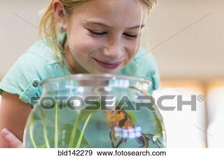 Stock Photo - Caucasian girl admiring pet goldfish in fishbowl. Fotosearch