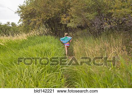 Stock Image - Caucasian girl carrying towel in tall grass. Fotosearch
