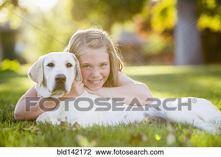 Stock Image - Caucasian girl hugging pet dog on grassy lawn. Fotosearch