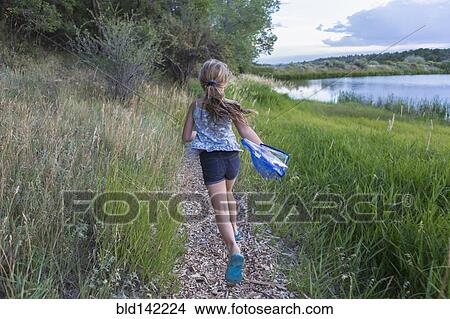 Picture - Caucasian girl running on path near tall grass. Fotosearch