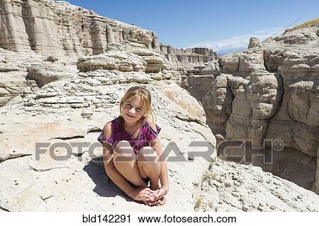 Stock Image - Caucasian girl sitting on rock formations. Fotosearch