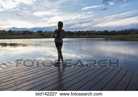 Stock Photo - Caucasian girl standing on wooden deck near lake. Fotosearch