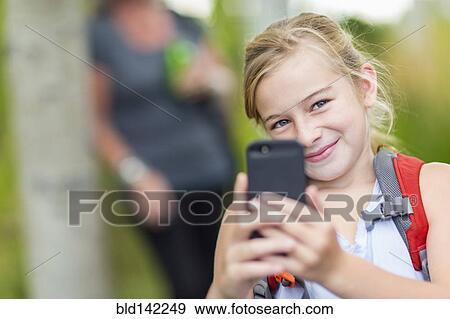 Stock Photo - Caucasian girl taking cell phone photograph in forest. Fotosearch