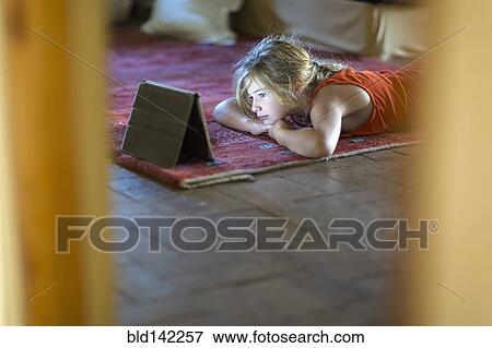 Stock Photo - Caucasian girl watching digital tablet on floor. Fotosearch