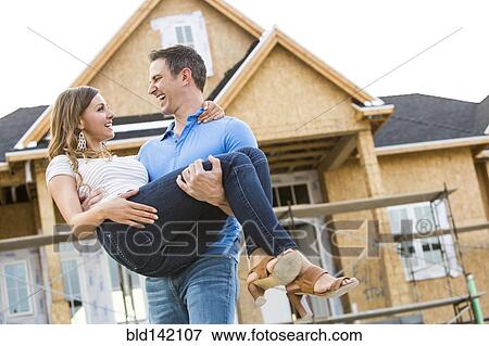 Stock Photo - Caucasian man carrying woman near house under construction. Fotosearch