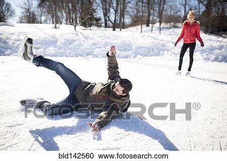Stock Image - Caucasian man falling while ice skating on frozen lake. Fotosearch