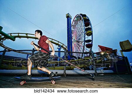 Picture - Caucasian man skateboarding with paddle pole at amusement park. Fotosearch