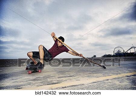 Caucasian man skateboarding with paddle pole at beach View Large Photo Image Stock Image - Caucasian man skateboarding with paddle pole at beach. Fotosearch