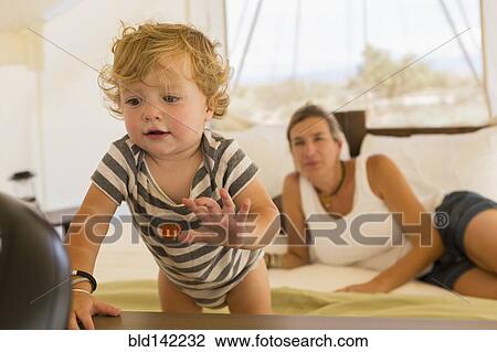 Stock Image - Caucasian mother watching baby son exploring. Fotosearch