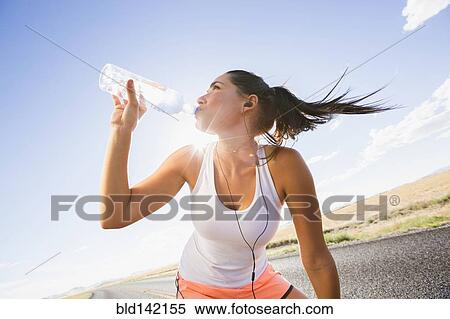 Stock Photography - Caucasian runner drinking water bottle on remote road. Fotosearch
