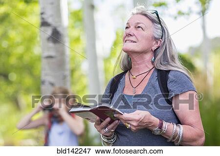 Stock Photo - Caucasian senior woman carrying guidebook in forest. Fotosearch