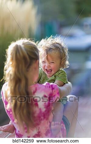 Stock Photo - Caucasian sister holding laughing baby brother outdoors. Fotosearch