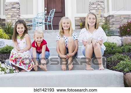 Stock Image - Caucasian sisters smiling on front stoop. Fotosearch
