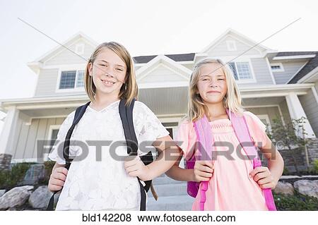 Stock Photo - Caucasian sisters with backpacks smiling near house. Fotosearch