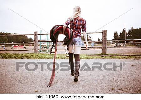 Caucasian woman carrying horse saddle on ranch View Large Photo Image Stock Image - Caucasian woman carrying horse saddle on ranch. Fotosearch