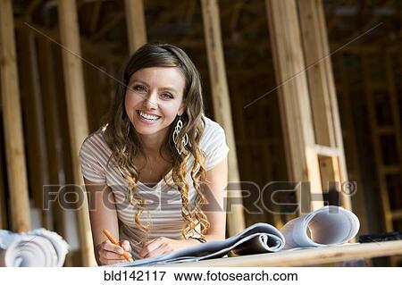 Stock Photo - Caucasian woman marking blueprints in house under construction. Fotosearch