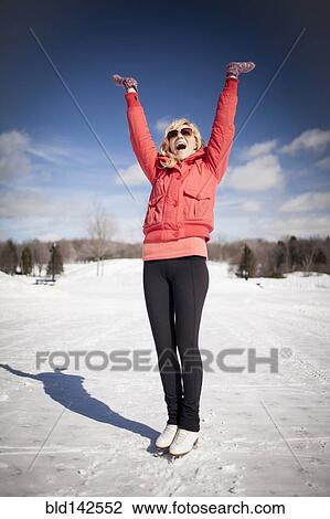 Stock Image - Caucasian woman on ice skates cheering on frozen lake. Fotosearch