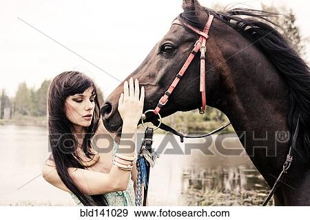 Stock Photo - Caucasian woman petting horse outdoors. Fotosearch