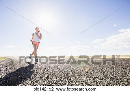 Stock Image - Caucasian woman running on remote road. Fotosearch