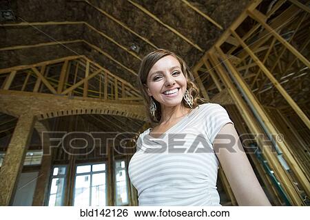 Stock Photograph - Caucasian woman smiling in house under construction. Fotosearch