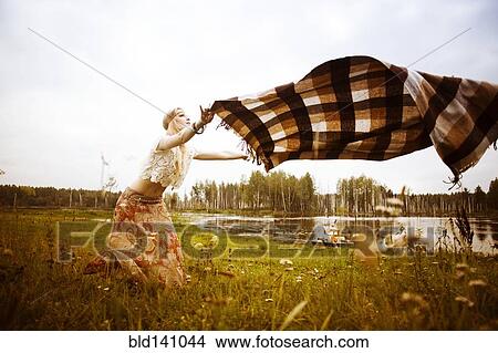 Picture - Caucasian woman spreading blanket in field. Fotosearch
