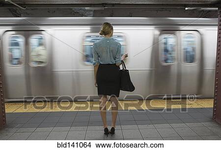 Picture - Caucasian woman standing near passing subway in train station. Fotosearch