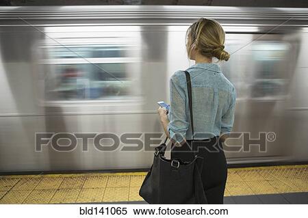 Stock Photography - Caucasian woman standing near passing subway in train station. Fotosearch