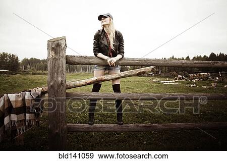 Stock Photo - Caucasian woman standing on wooden fence at ranch. Fotosearch