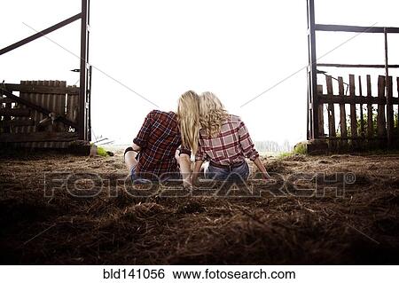 Stock Photograph - Caucasian women sitting on hay in barn. Fotosearch