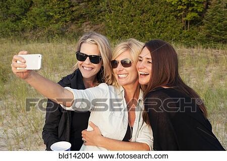 Caucasian women taking cell phone photograph outdoors View Large Photo Image Picture - Caucasian women taking cell phone photograph outdoors. Fotosearch