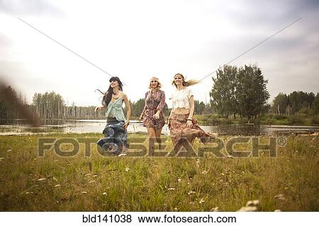 Stock Photo - Caucasian women walking in field near lake. Fotosearch