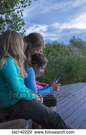 Stock Photo - Children using cell phone together outdoors. Fotosearch