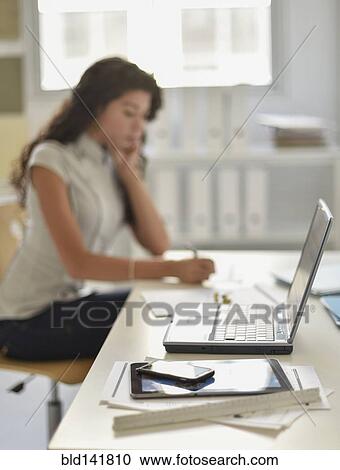 Stock Image - Close up of cell phone, digital tablet and laptop on desk of mixed race businesswoman. Fotosearch