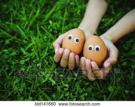 Stock Image - Close up of mixed race girl holding eggs with googly eyes. Fotosearch