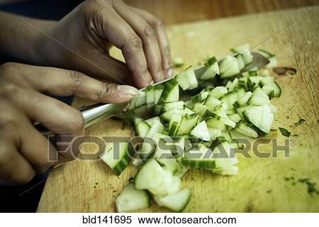Stock Photography - Close up of mixed race woman chopping cucumber in kitchen. Fotosearch